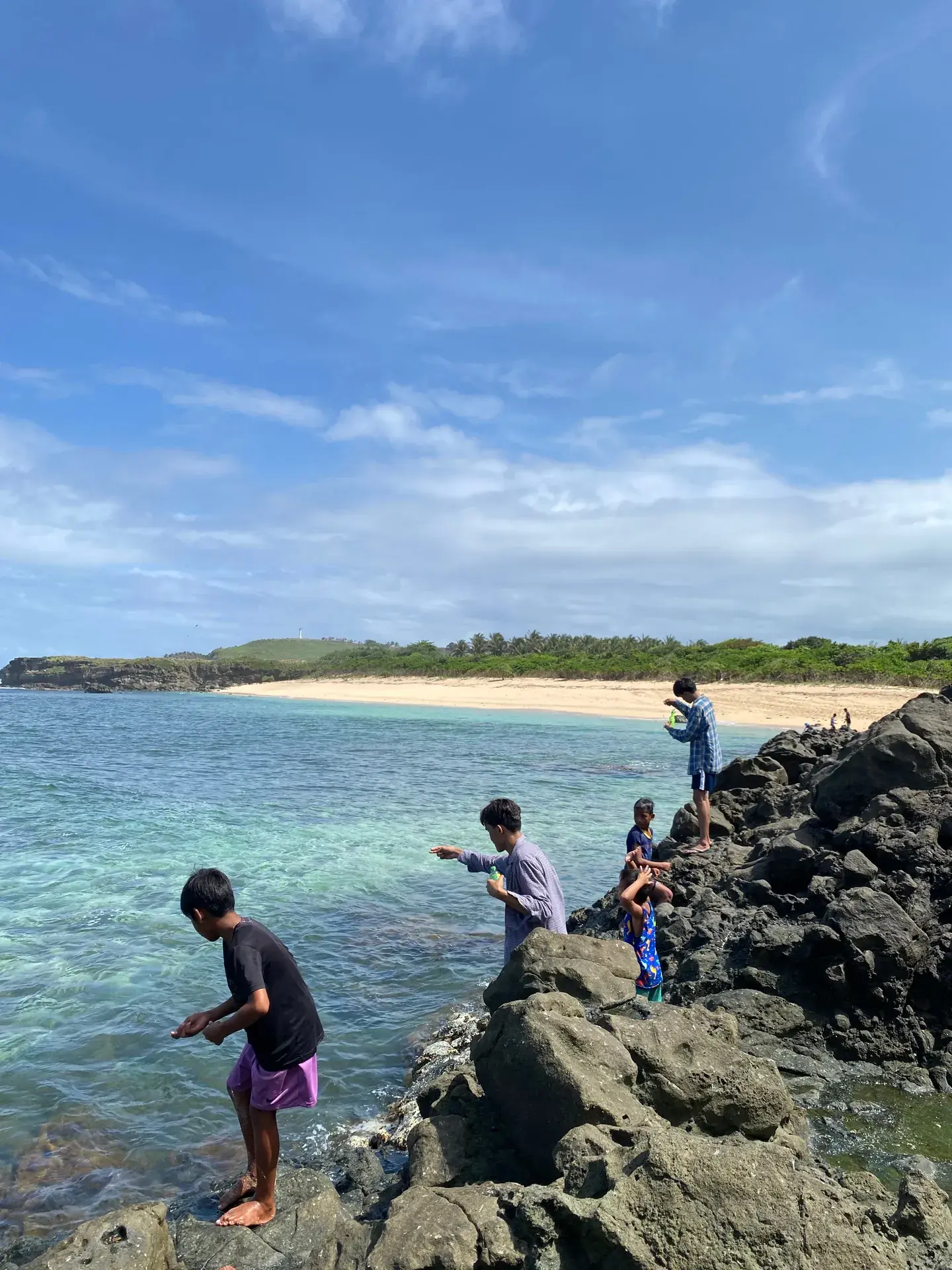 Locals on volcanic rocks above clear water on a Bicol coast