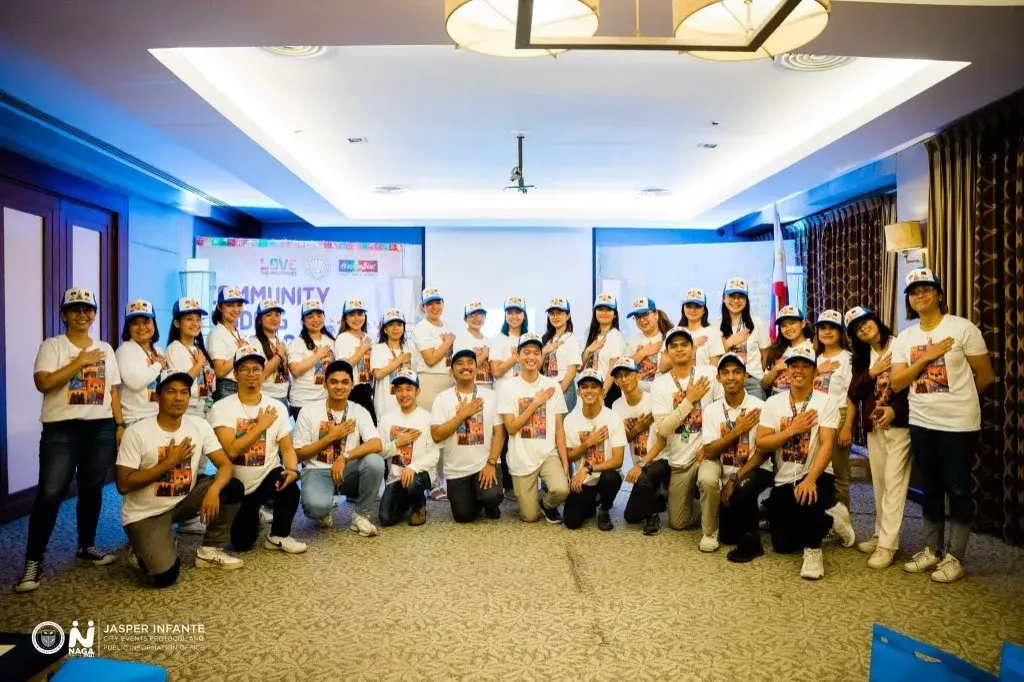 A large group in matching shirts and caps gathered for a community event indoors, with a Philippine flag beside them